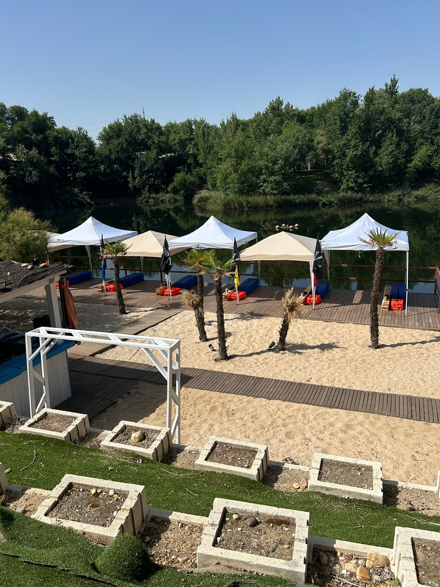 Playa fluvial con carpas y palmeras junto a un lago, escenario de la fiesta de verano del equipo