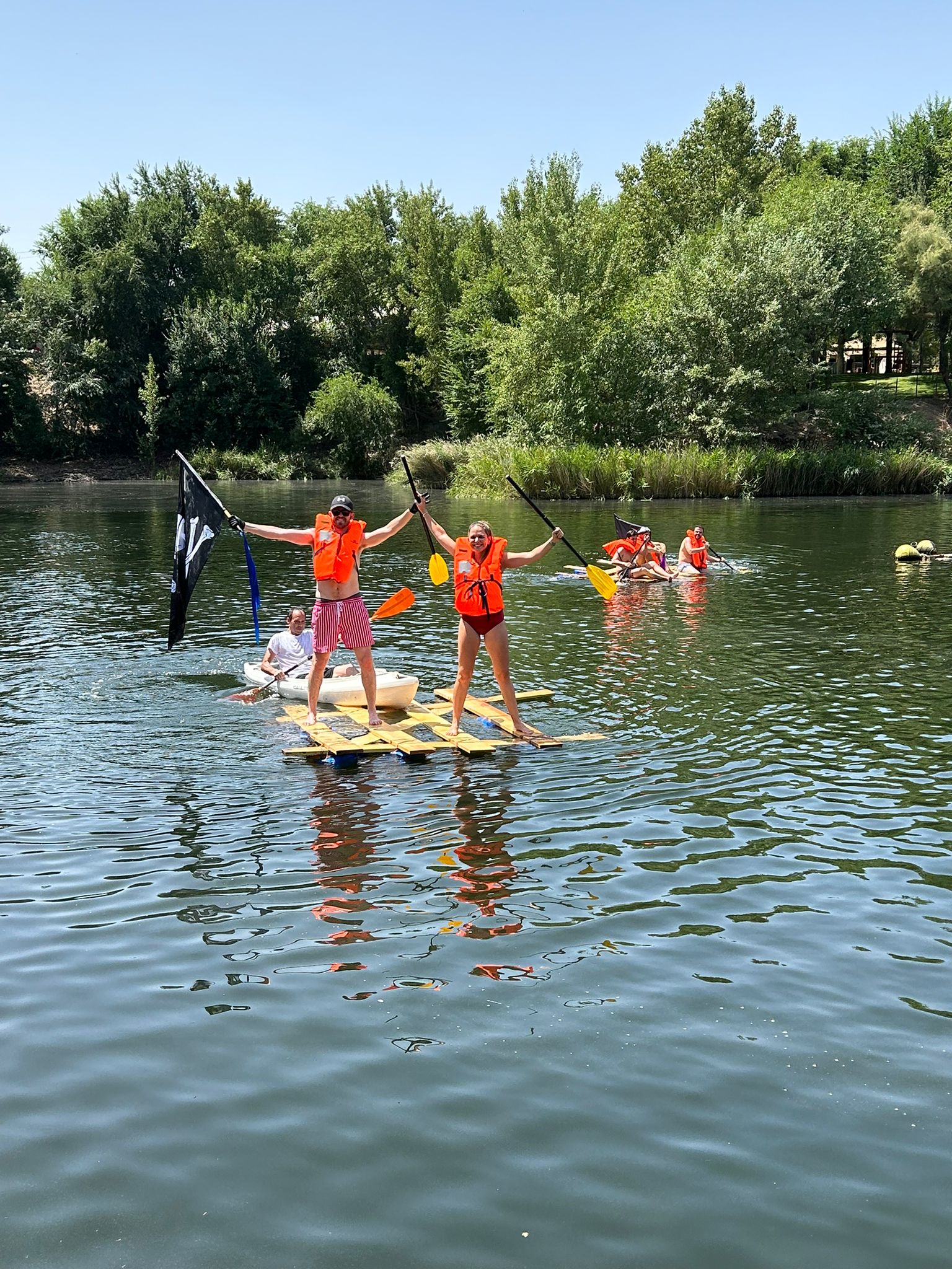Dos compañeros con chaleco salvavidas celebran sobre una balsa casera flotando en el lago
