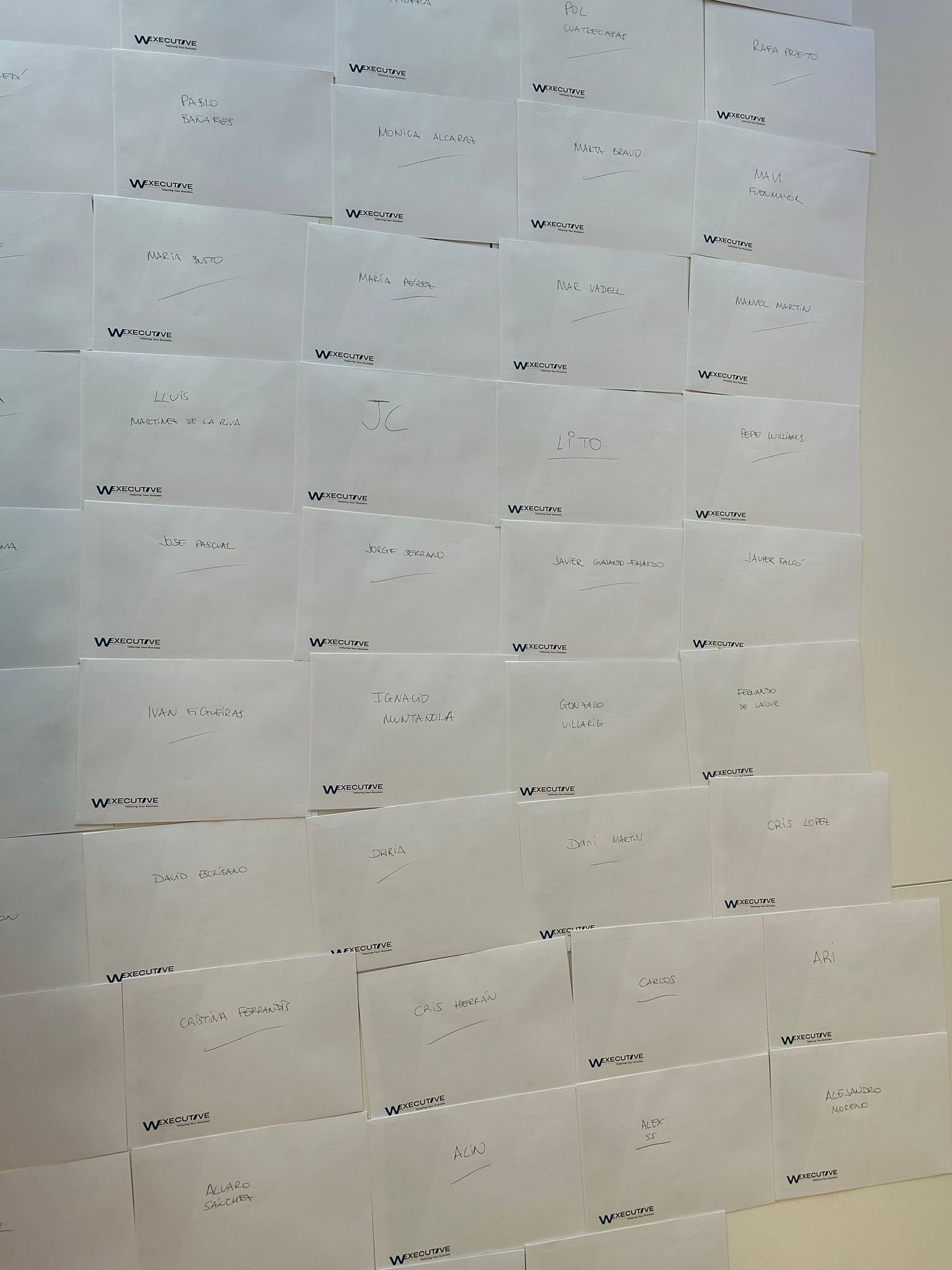 Pared cubierta de sobres con membrete W Executive y el nombre manuscrito de cada miembro del equipo