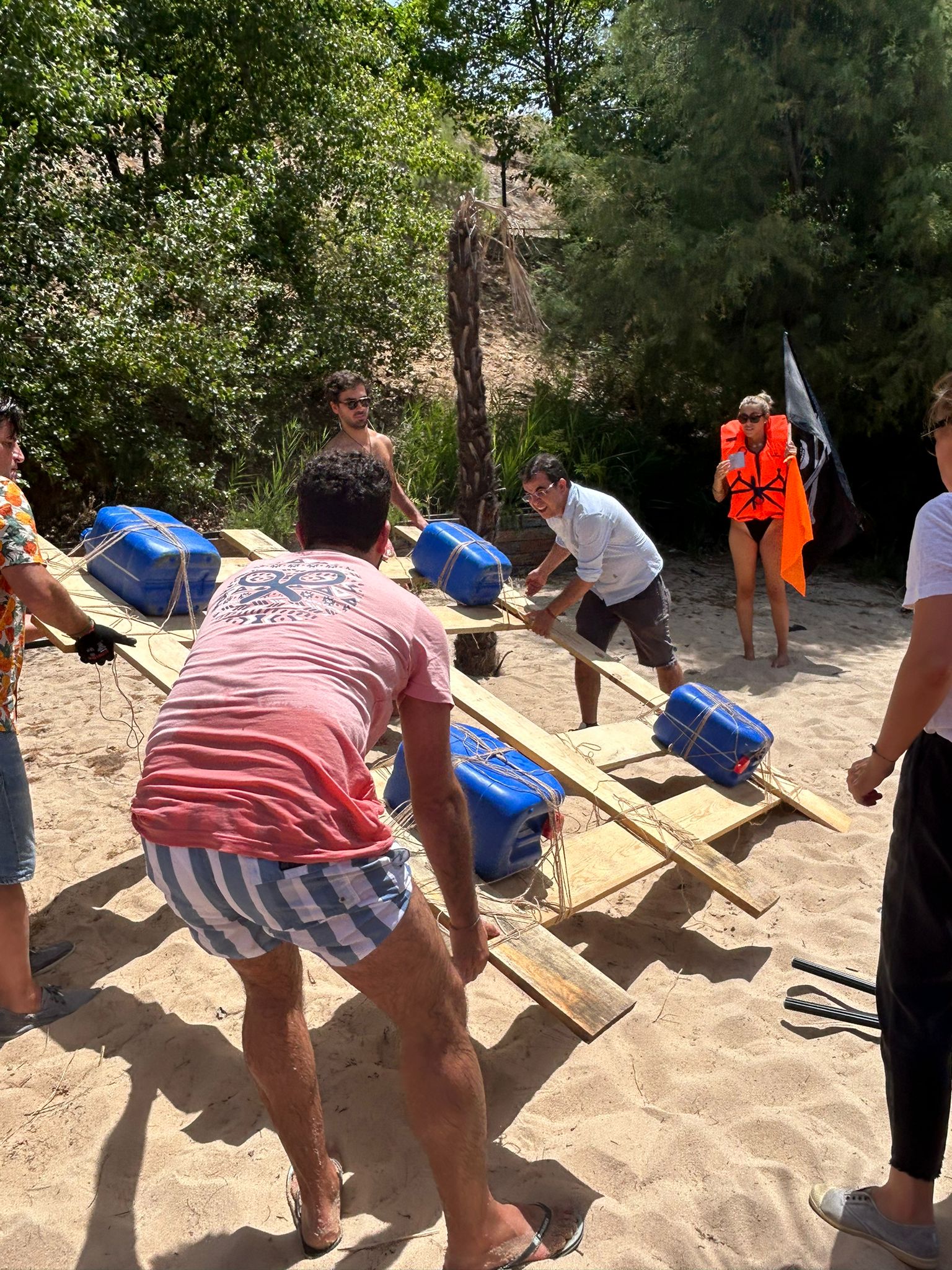 Compañeros construyen en la playa una balsa con tablas y bidones para la prueba de equipo