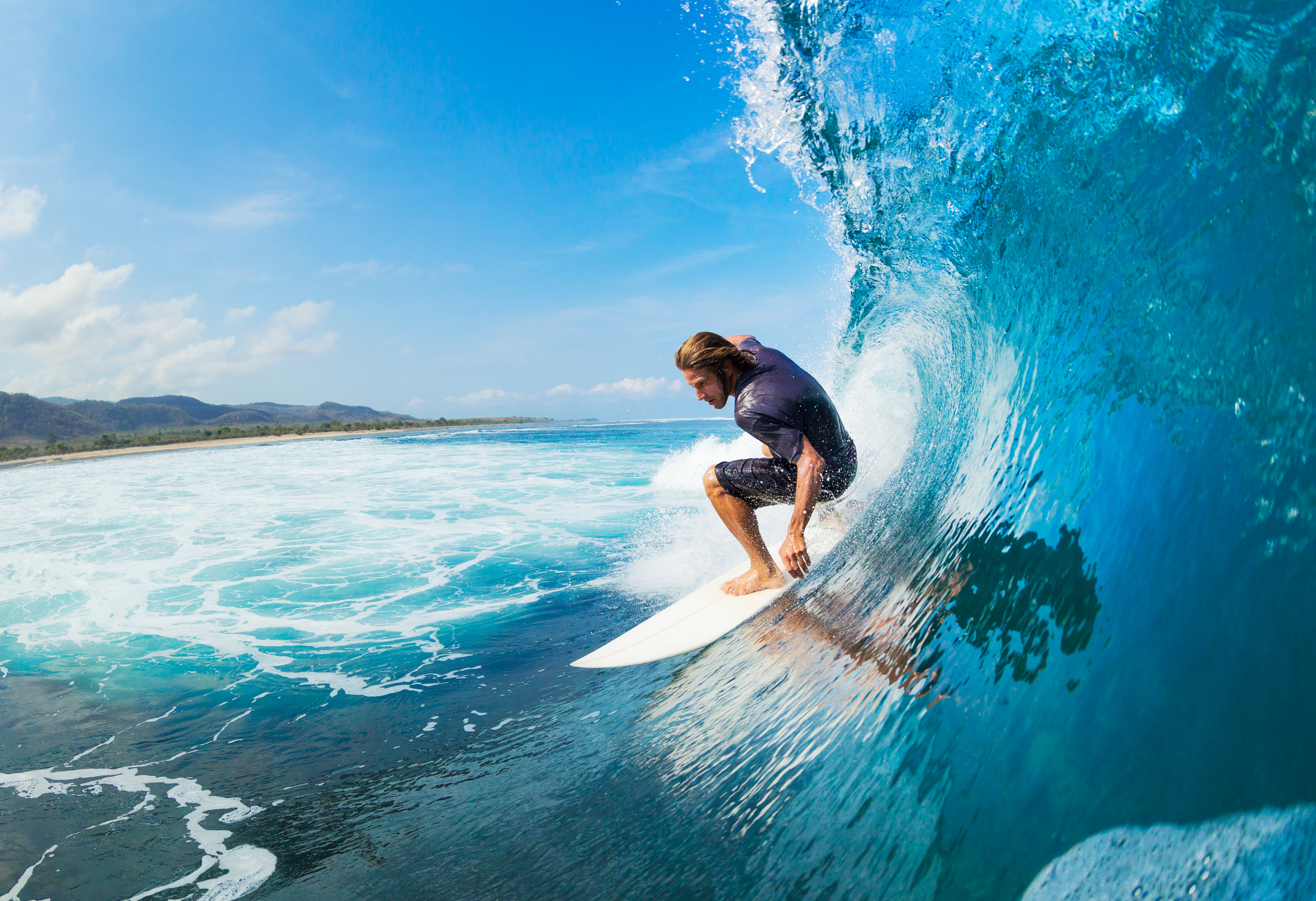 Surfista cabalgando el tubo de una gran ola azul junto a la costa