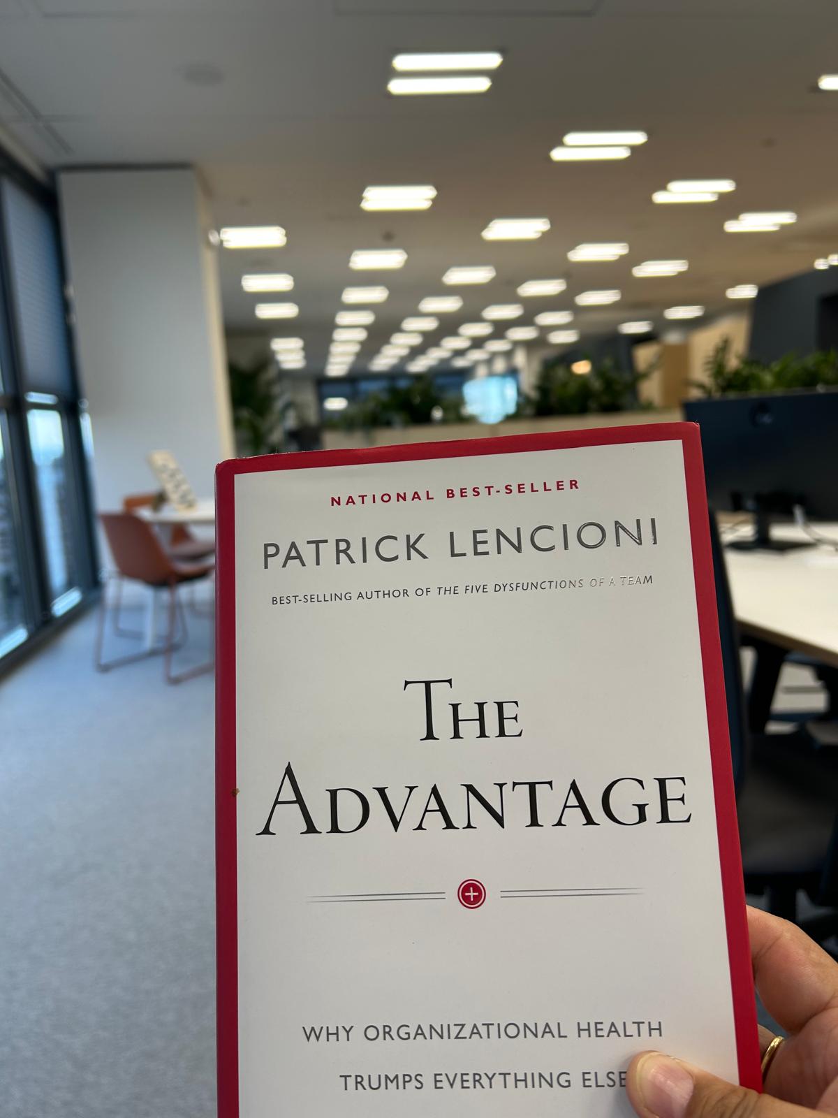 Libro The Advantage de Patrick Lencioni sostenido en una oficina diáfana