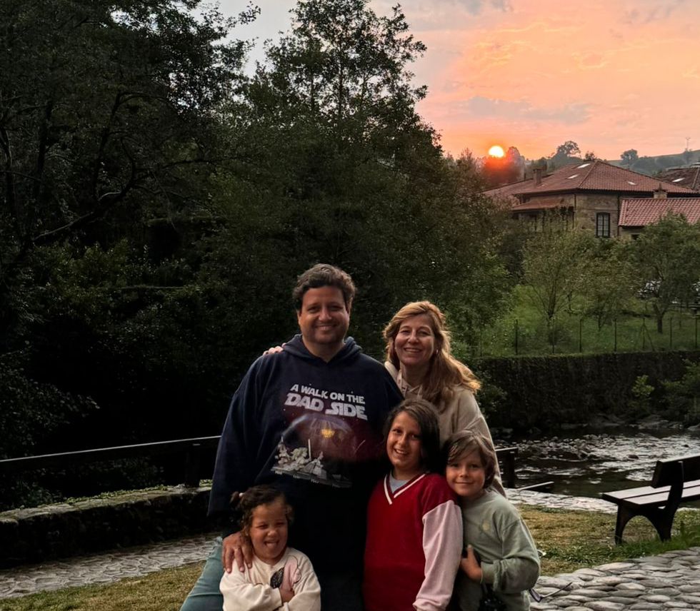 Familia de cinco posando junto a un río al atardecer en un entorno rural verde