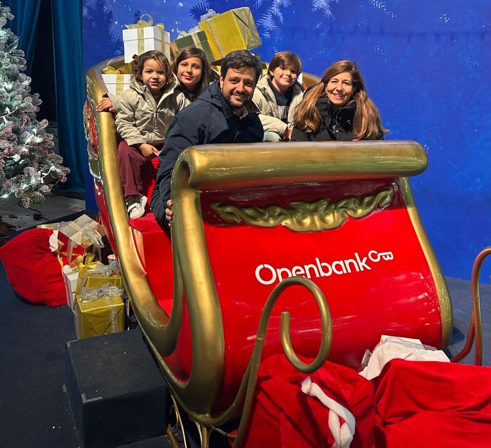 Familia de cinco posando en un trineo navideño rojo de Openbank rodeado de regalos