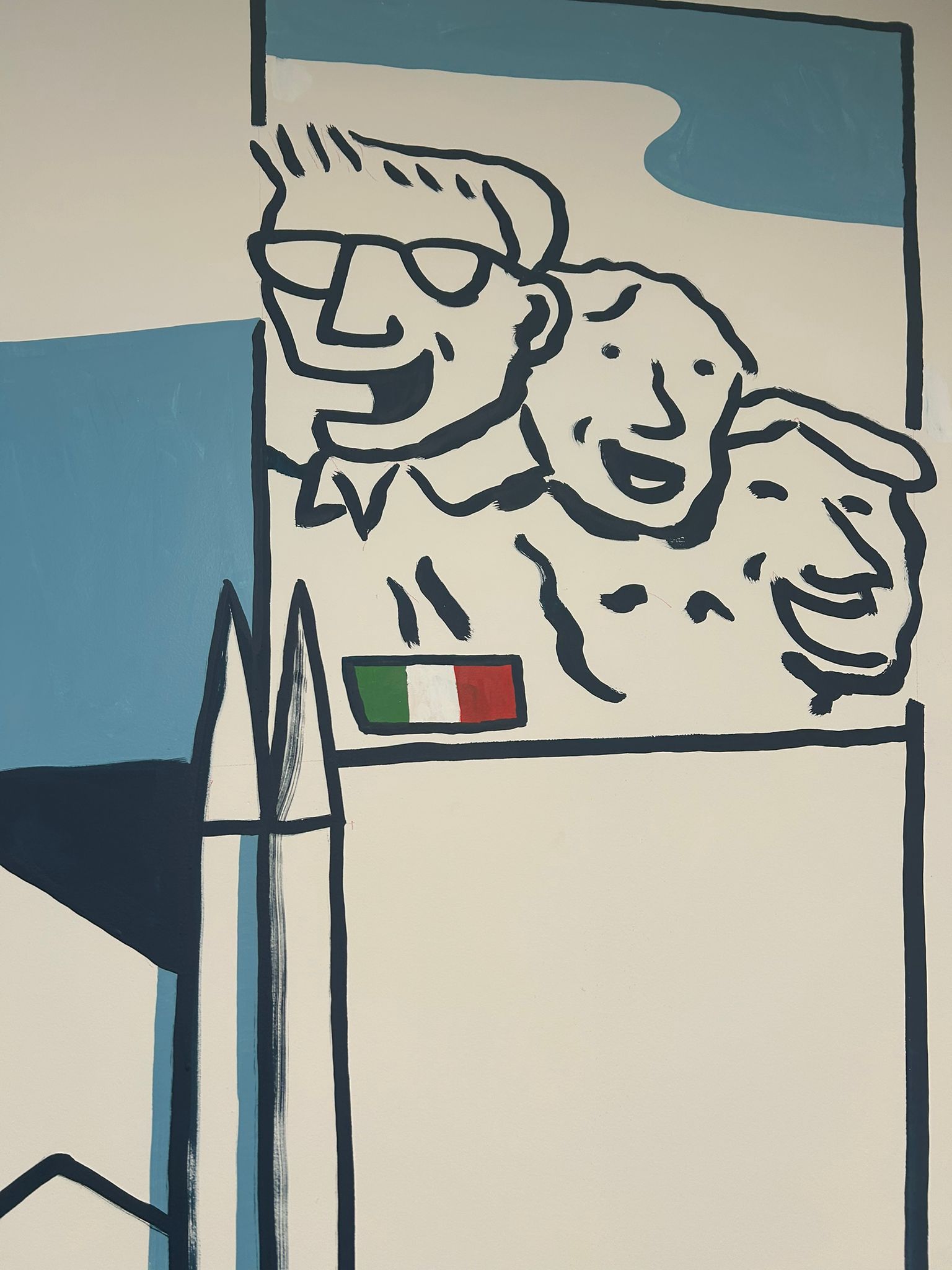 Detalle del mural tipo Monte Rushmore con los rostros del board global de W y la bandera italiana